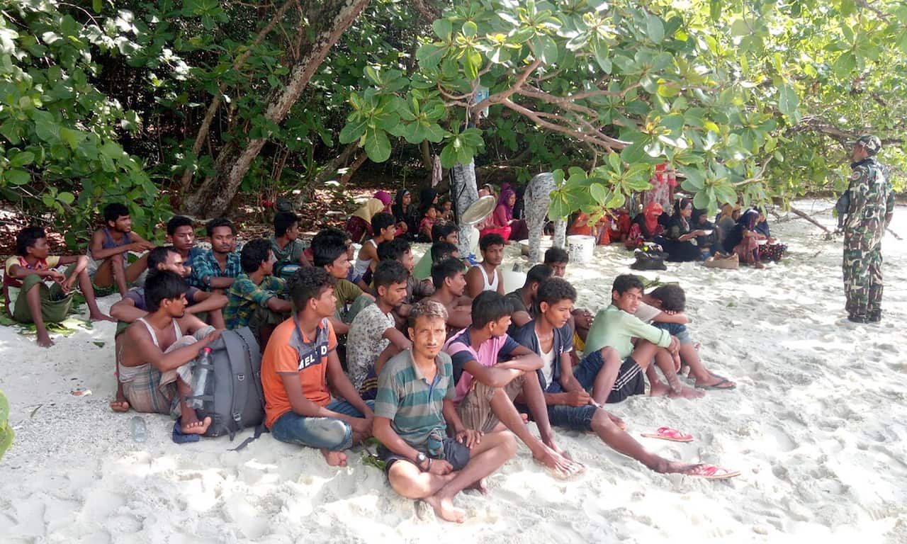 Thai security officials stand guard as they provide food to Rohingya refugees.