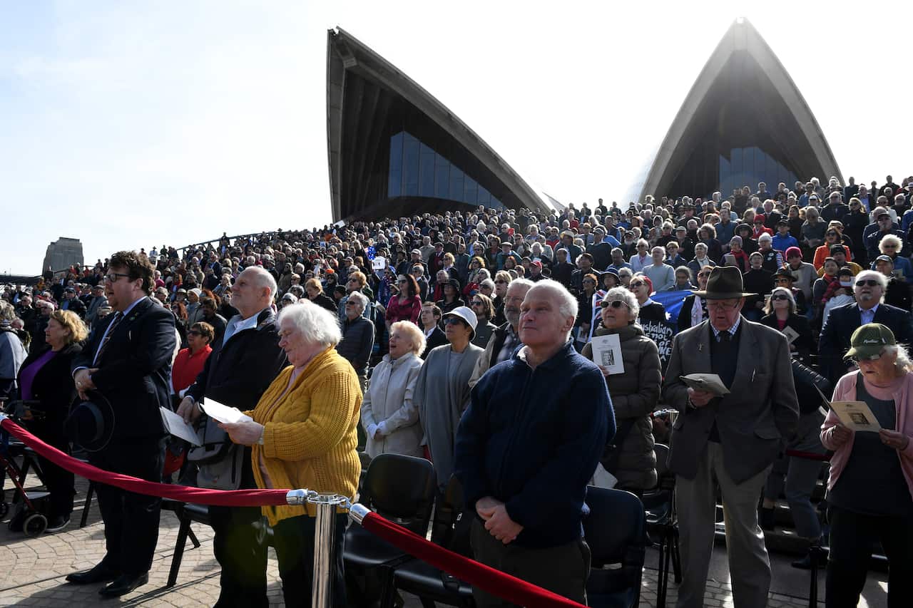 Members of the public stand for the national anthem as they watch the service from the steps of the Sydney Opera House.