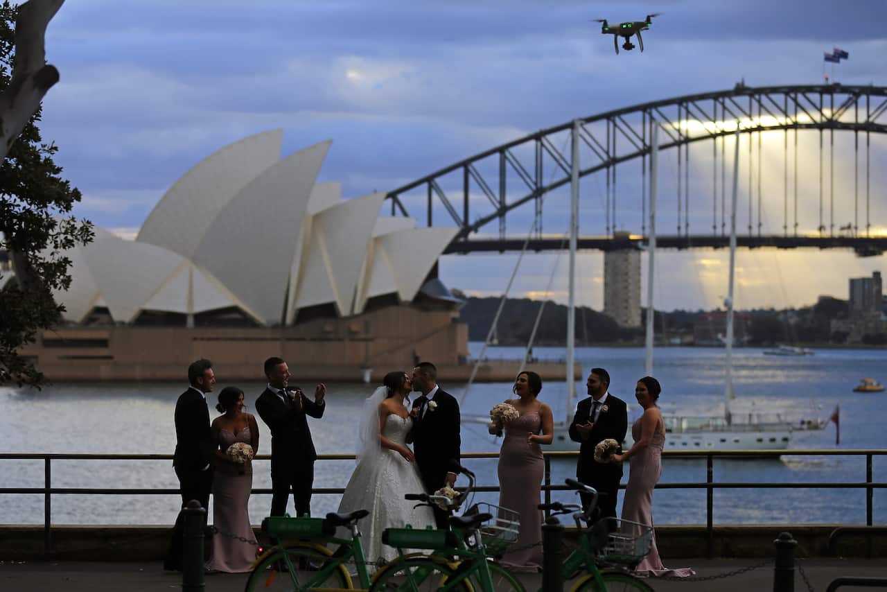 The Sydney Harbour Bridge and the Sydney Opera House are seen as a wedding party takes photos during the winter solstice in Sydney, Saturday, June 22, 2019. (AAP Image/Steven Saphore) NO ARCHIVING