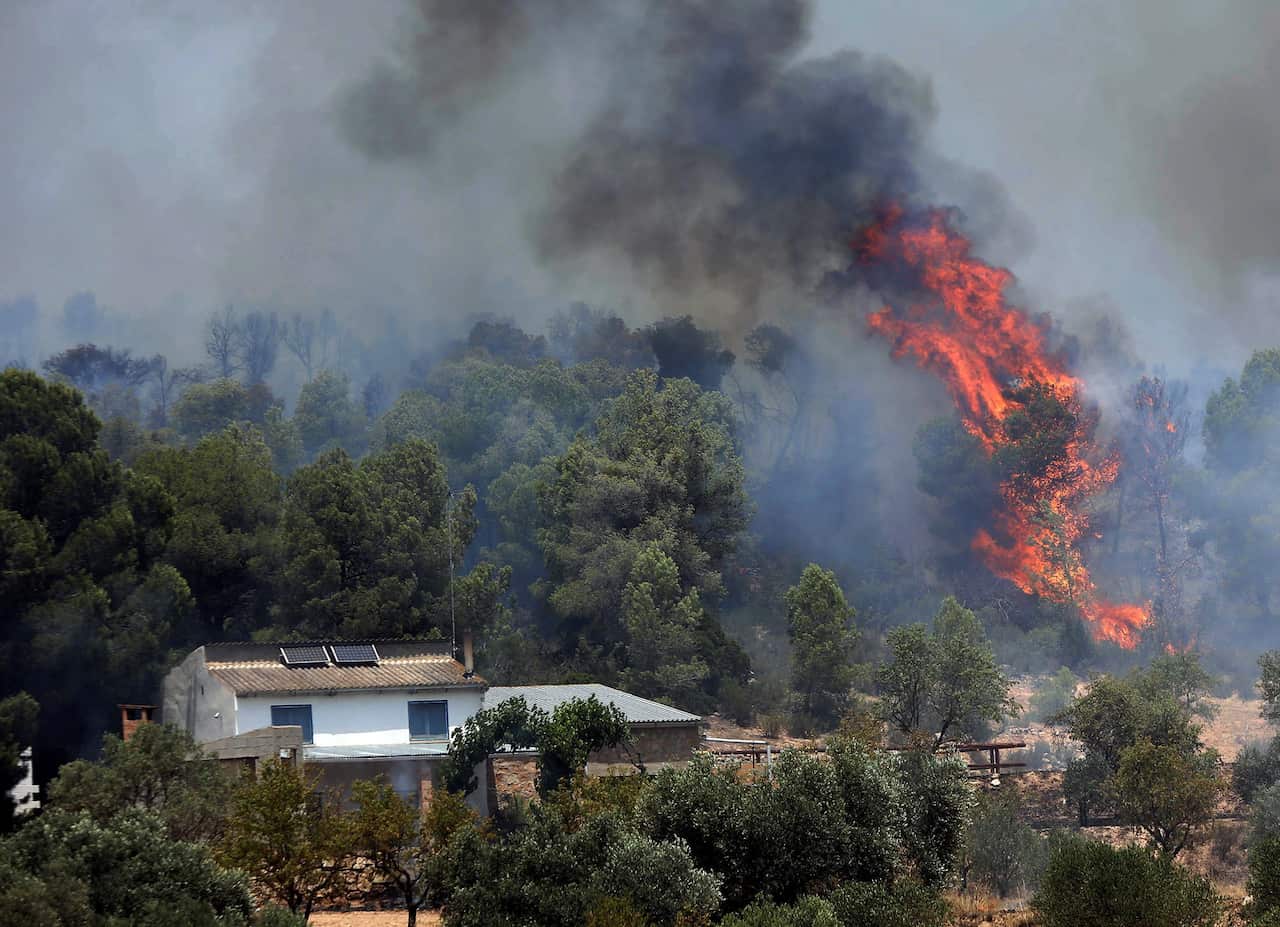 epa07677412 Fire and smoke rise near a house during a forest fire in La Torre de l'Espanyol in Tarragona, Spain, 27 June 2019. Fire emergency teams work to control the flames that have already burnt 4,00 hectares of land. EPA/JAUME SELLART