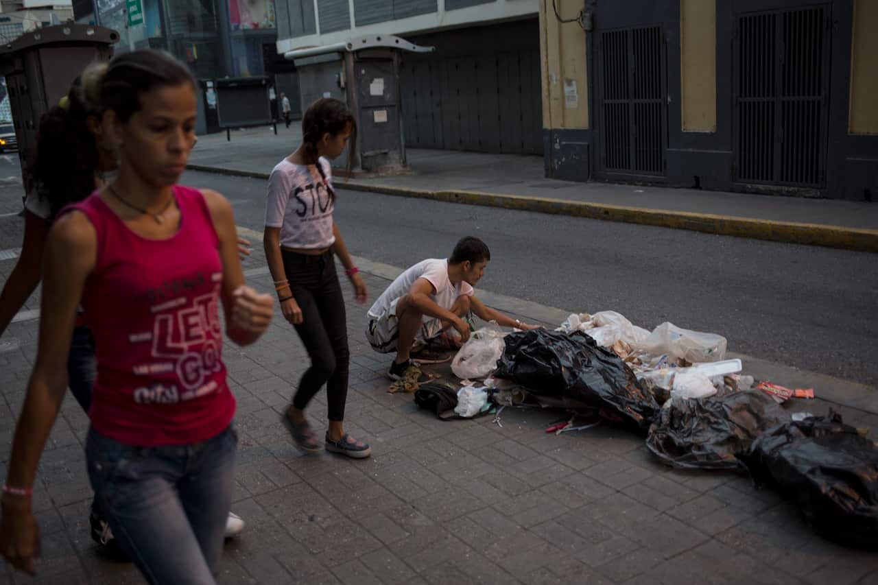A man searches for food in the trash, on a sidewalk in Caracas, Venezuela.
