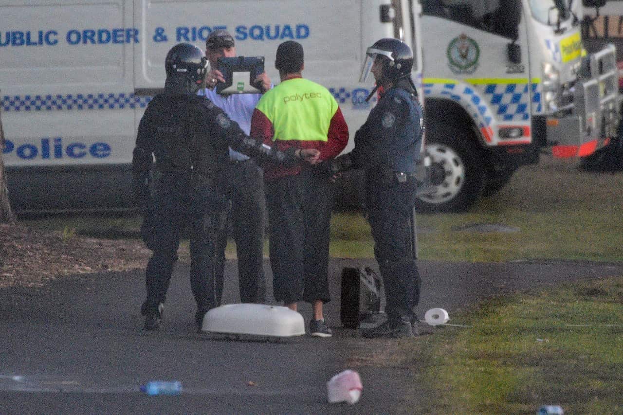 Riot police lead a detainee away in handcuffs during a riot at the Frank Baxter Juvenile Justice Centre.