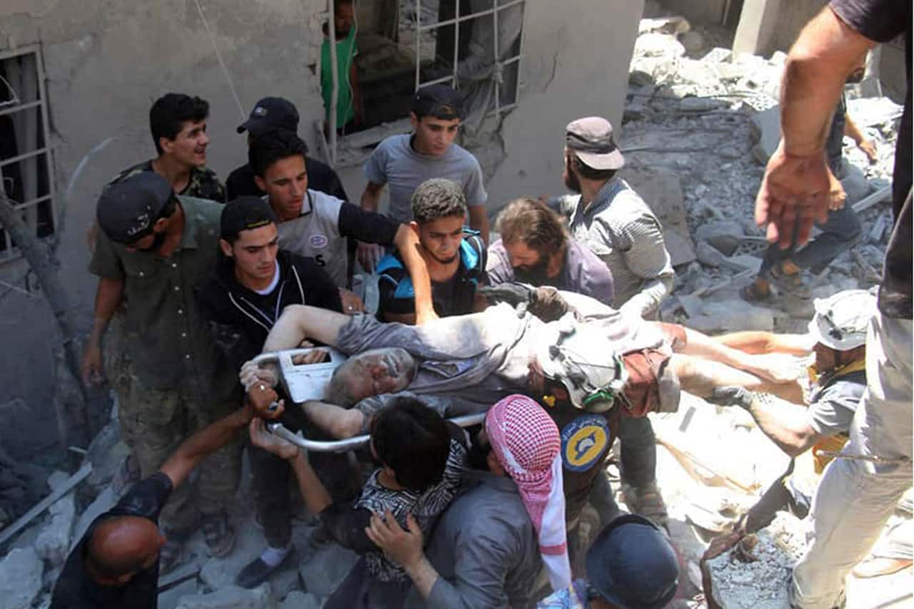 This photo provided by the Syrian Civil Defense White Helmets shows defense workers and civilians carry an injured man after an airstrike hit Ariha, Syria.