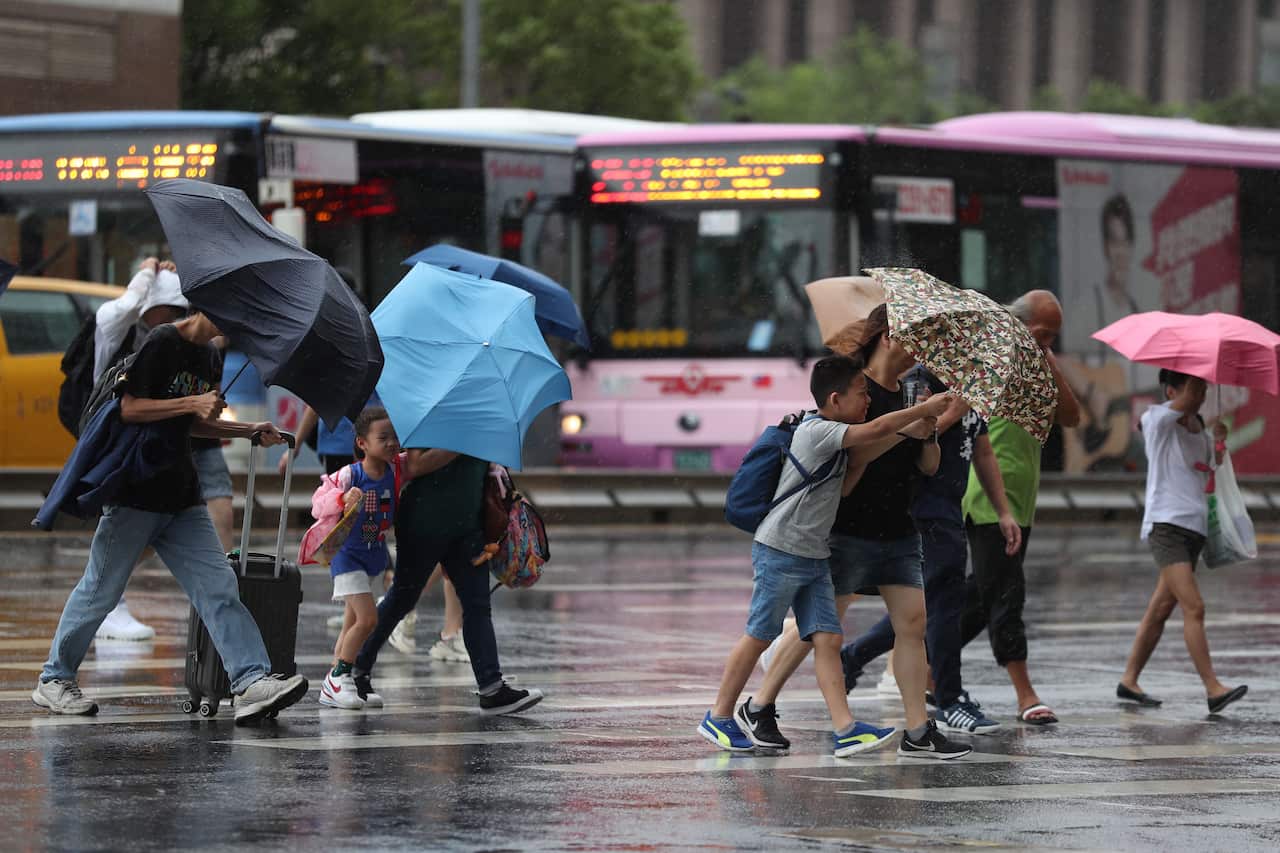 People cross a street during downpour and strong winds brought by Typhoon Lekima in Taipei, Taiwan.