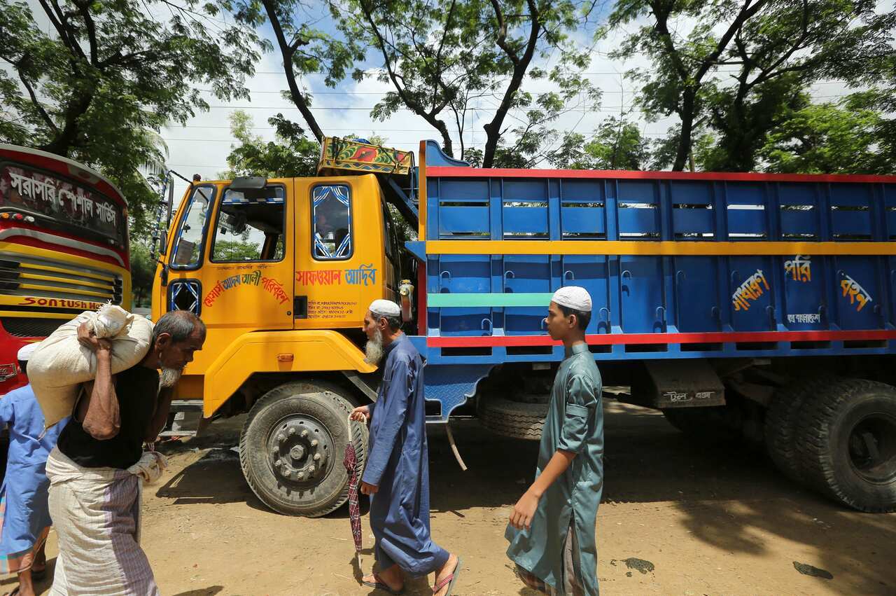 Rohingya refugees walk past trucks that were brought to take them to Myanmar.