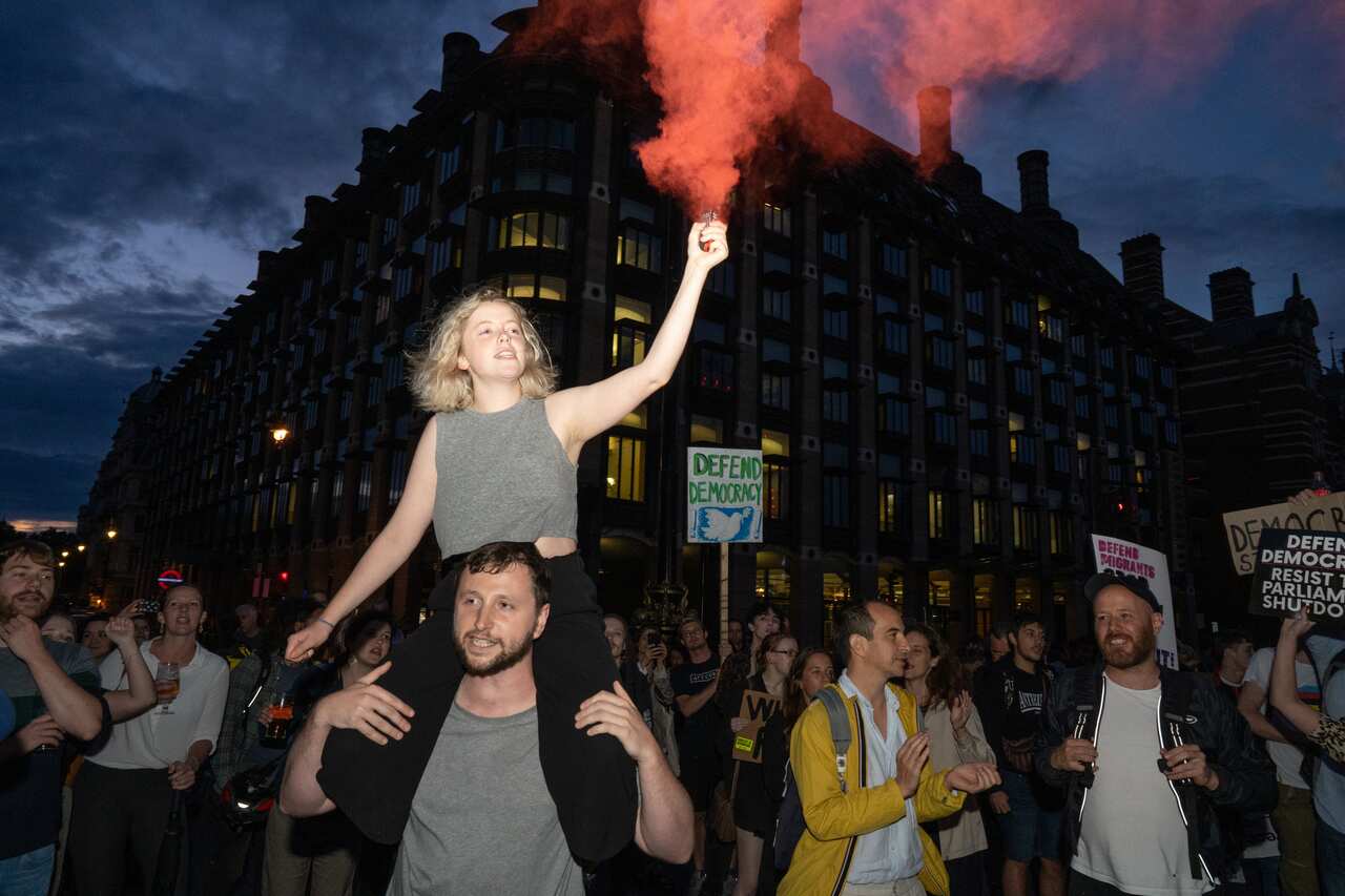 A woman is seen with a flare outside the houses of parliament where hundreds of people are seen protesting against Boris Johnson.