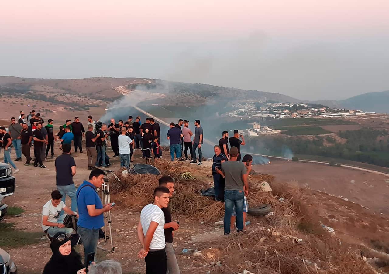 Lebanese journalists and villagers watch as Israeli army shells cause fires on the southern Lebanese border village of Maroun Al-Ras