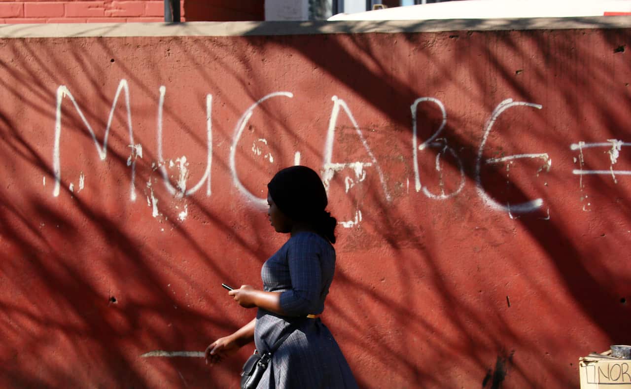  A woman walks past a  graffiti sign with Mugabes name on the streets of Harare.