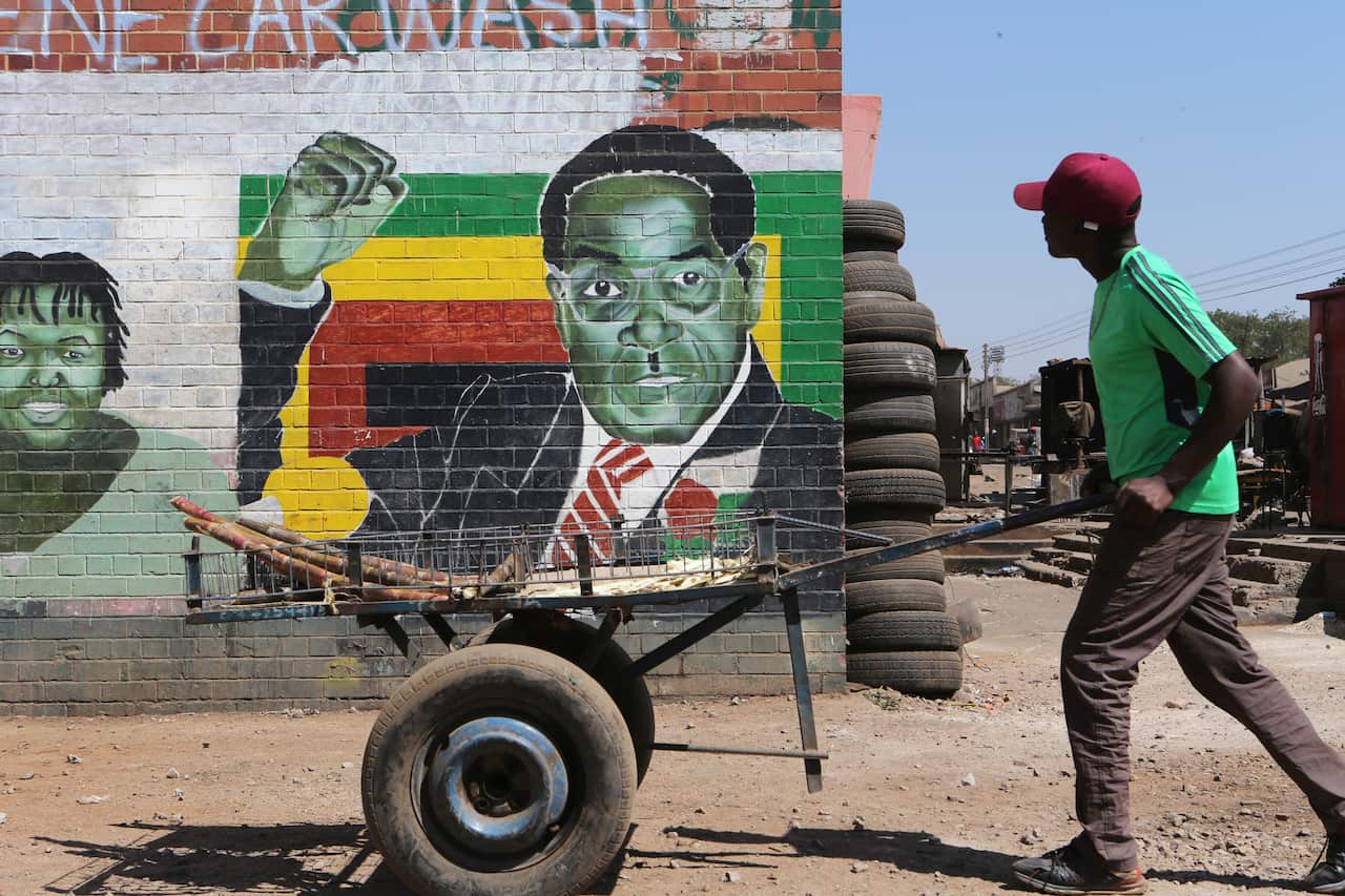 A man pushes an empty cart past a portrait of former Zimbabwean President Robert Mugabe.