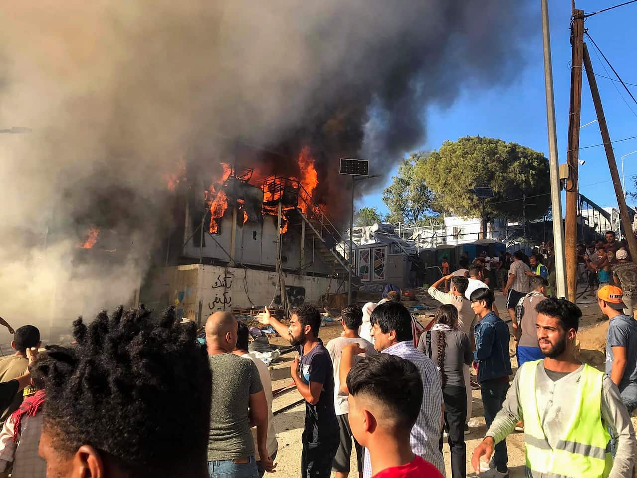 Migrants and refugees stand next to burning house containers at the Moria refugee camp on Lesbos.