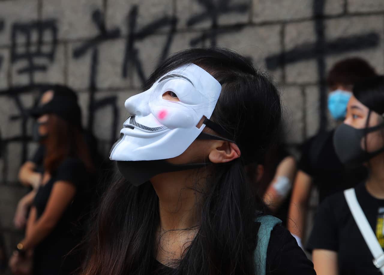 A woman wearing a Guy Fawkes mask stands with other protesters.