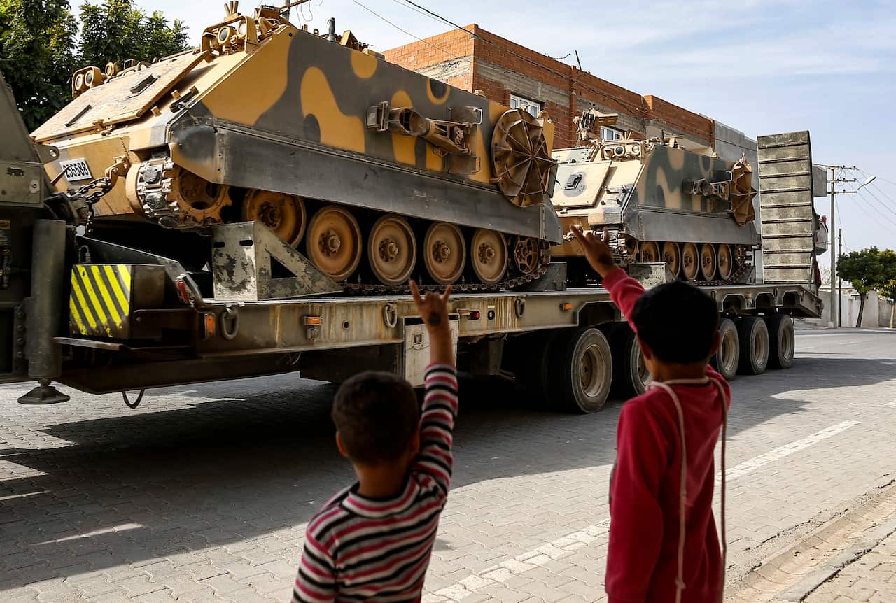 Children wave to a Turkish forces truck transporting armoured personnel carriers at the border with Syria in Karkamis, Gaziantep province, southeastern Turkey.