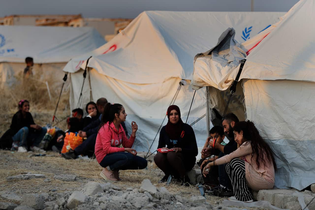 Syrians, displaced by the Turkish military operation in northeastern Syria, wait to receive tents and aid supplies at the Bardarash refugee camp in Iraq.
