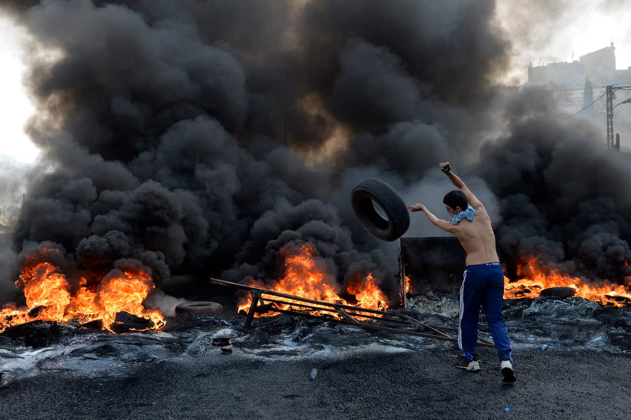 A protester throws a tire on the fire blocking the highway.