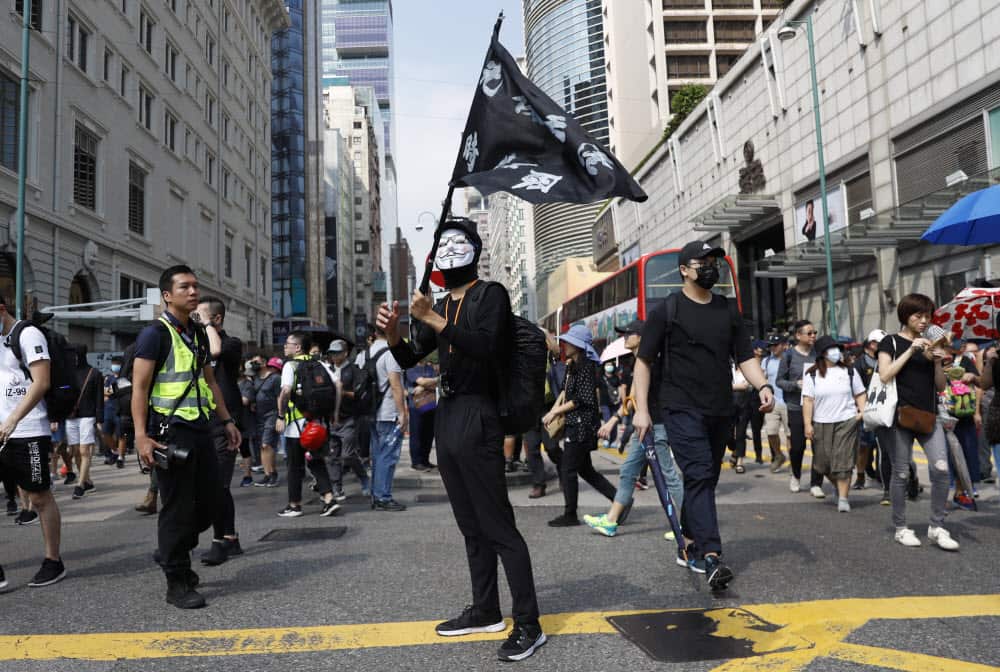 A protester wearing a Guy Fawkes mask holds a flag during a rally in Hong Kong on Sunday