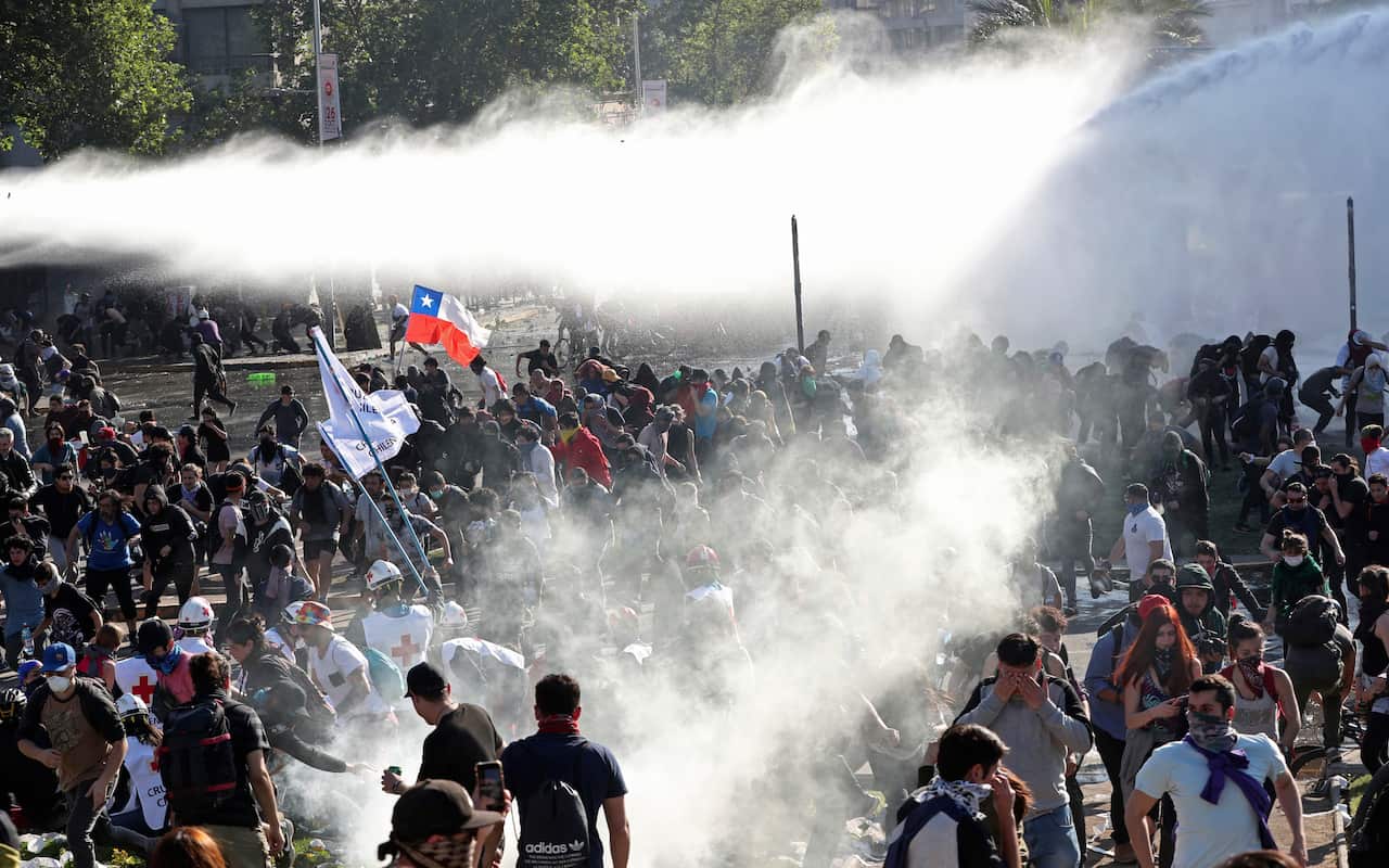 Demonstrators clash with police launching tear gas as a state of emergency remains in effect in Santiago.