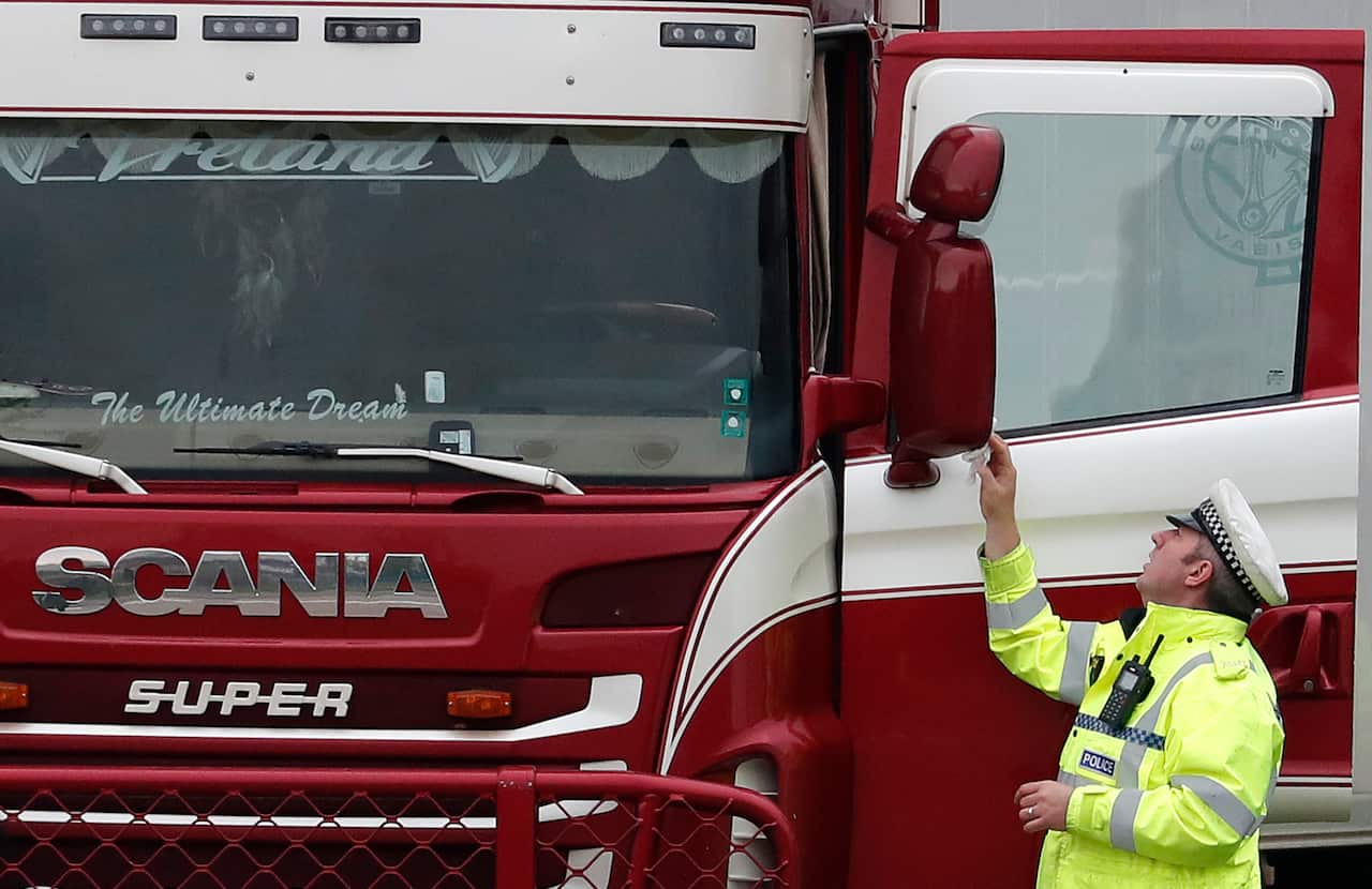 A police officer wipes the wing mirror of a truck that was found to contain a large number of dead bodies, in Thurrock, South England, Wednesday Oct. 23, 2019.