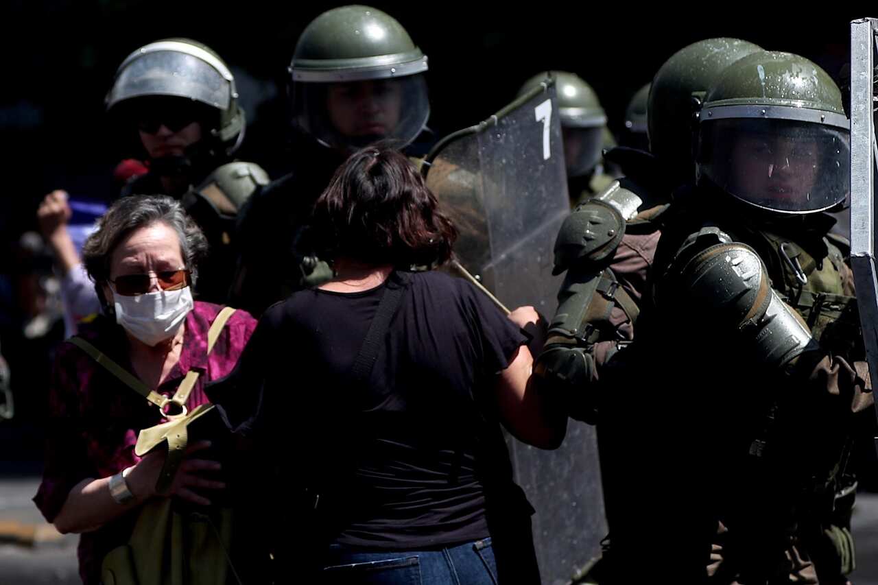 Two women demonstrate next to a group of police during the sixth day of protests against the Government, in Santiago, Chile.