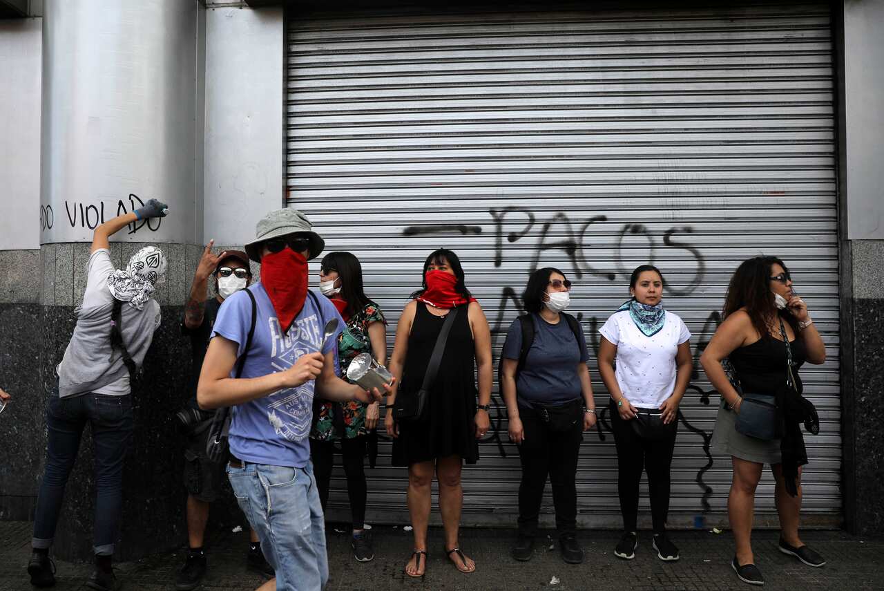 A demonstrator defaces a column as other protesters stand on the sidewalk during clashes with police in Santiago, Chile.