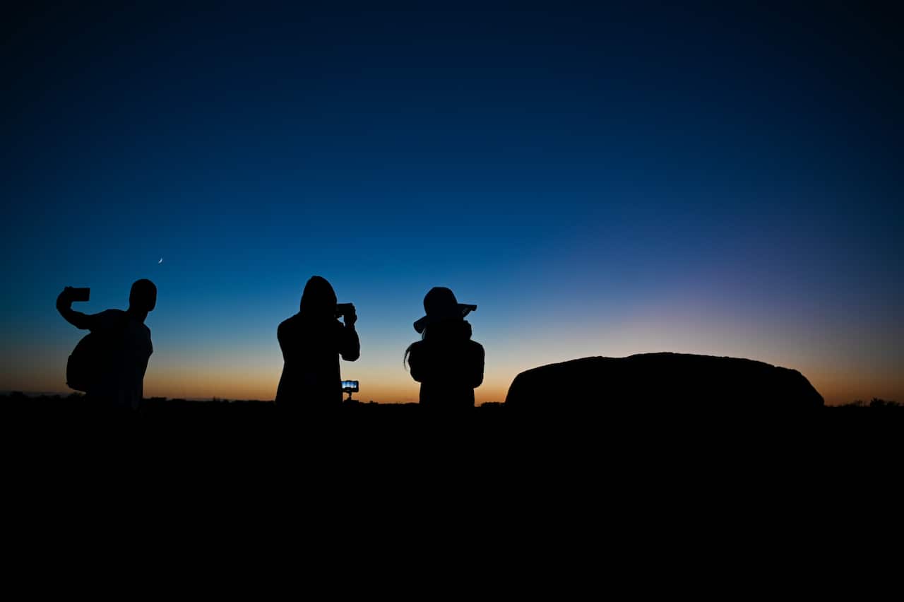 Tourists take pictures of Uluru, also known as Ayers Rock just before sunrise at Uluru-Kata Tjuta National Park in the Northern Territory, Saturday, October 26, 2019. (AAP Image/Lukas Coch) NO ARCHIVING