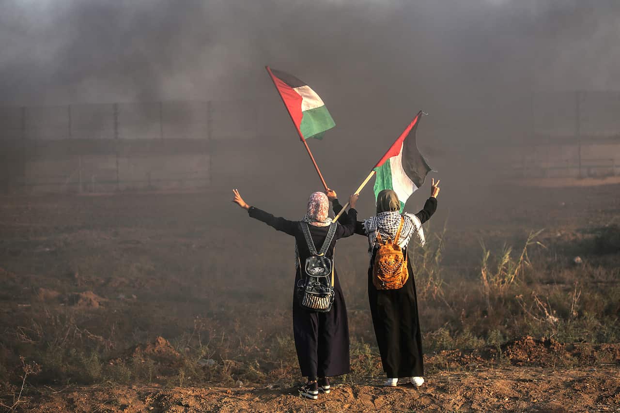 Protesters wave Palestinian flags next to Israeli troops during clashes near the border.