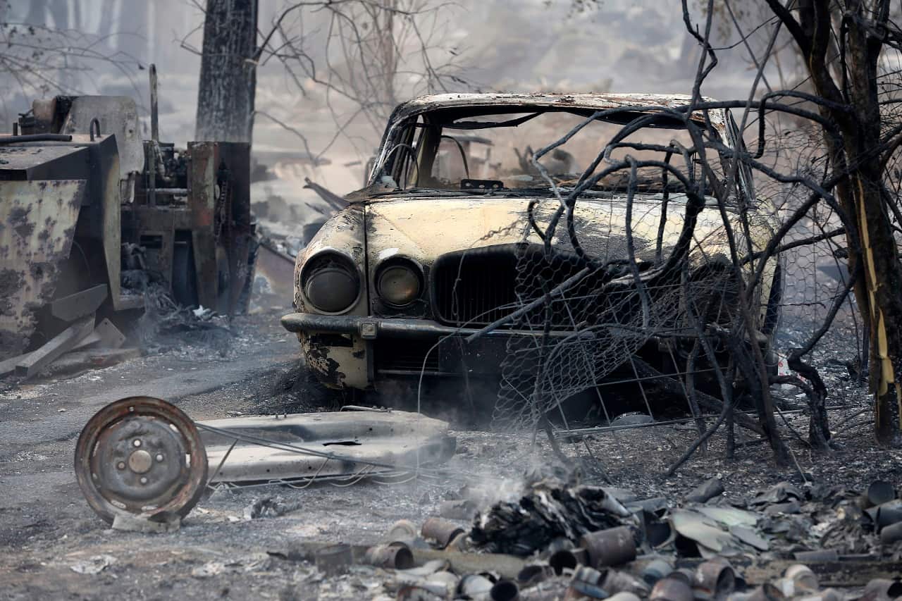 The burnt out shell of a Jaguar vehicle sits in the ruins of a smouldering house near Taree.