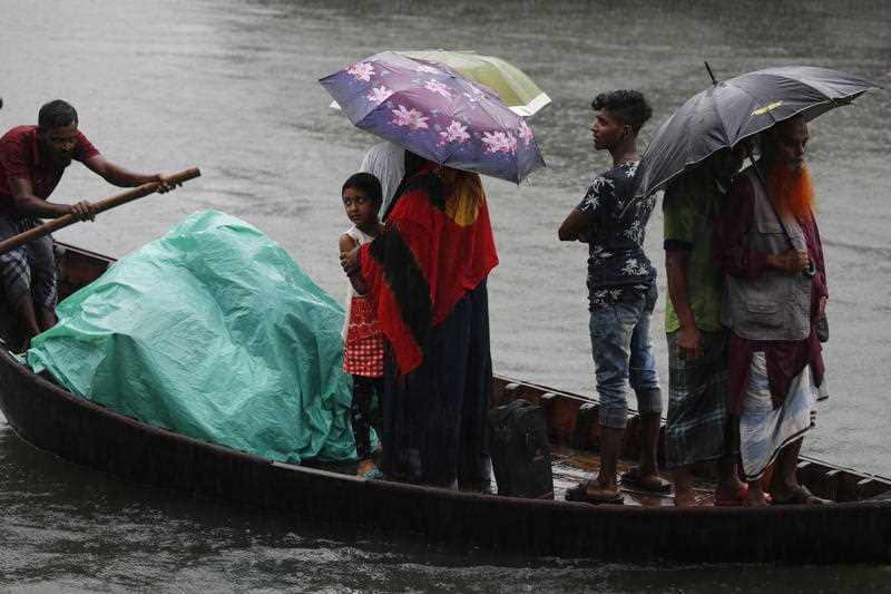 Bangladeshi passengers cover themselves with a plastic sheet and umbrellas 