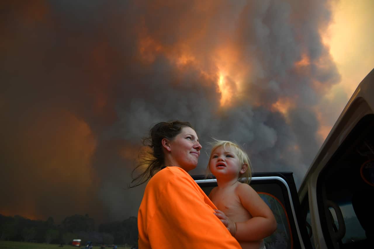 Sharnie Moren and her 18-month-old daughter Charlotte look on as thick smoke rises from bushfires near Coffs Harbour. 