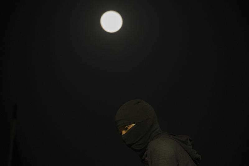 A protester with his face covered up is seen as the moon shines over the barricaded bridge leading into the Chinese University of Hong Kong