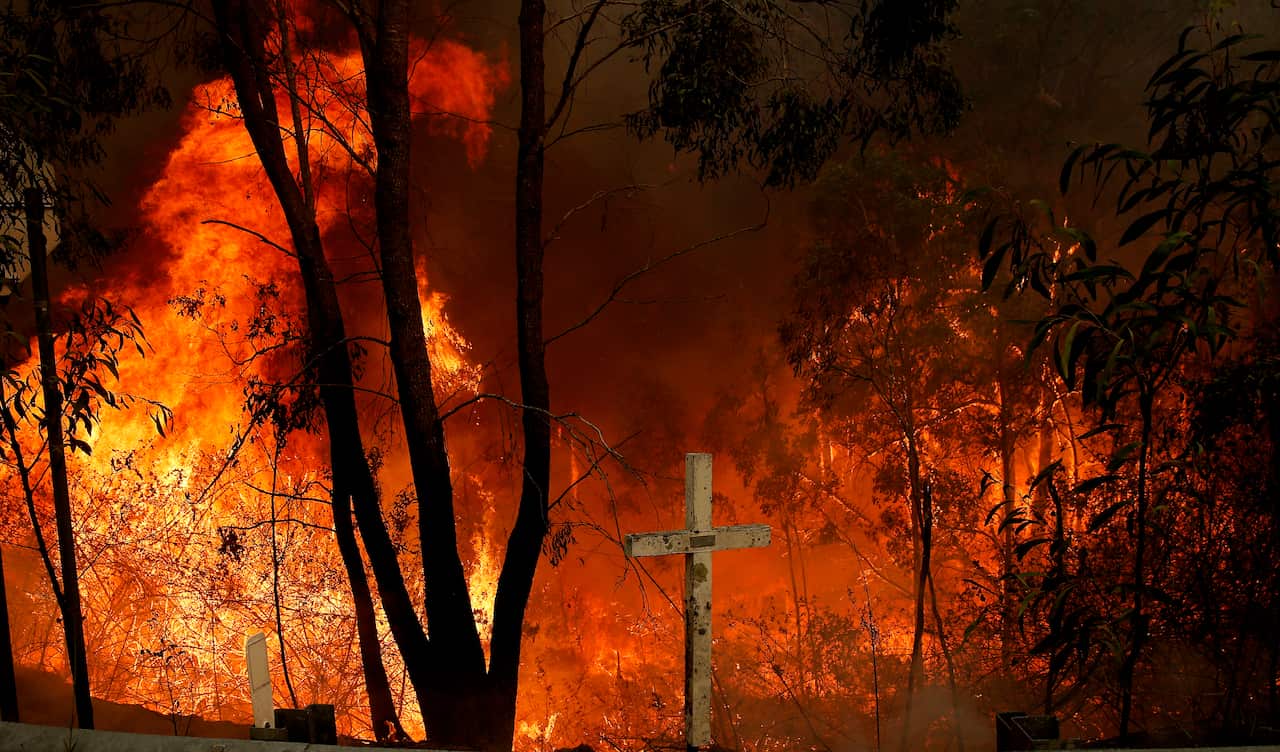 The Hillville bushfire burns out of control behind a memorial cross on the Pacific Highway at Possum brush south of Taree in the Mid North Coast region of NSW.