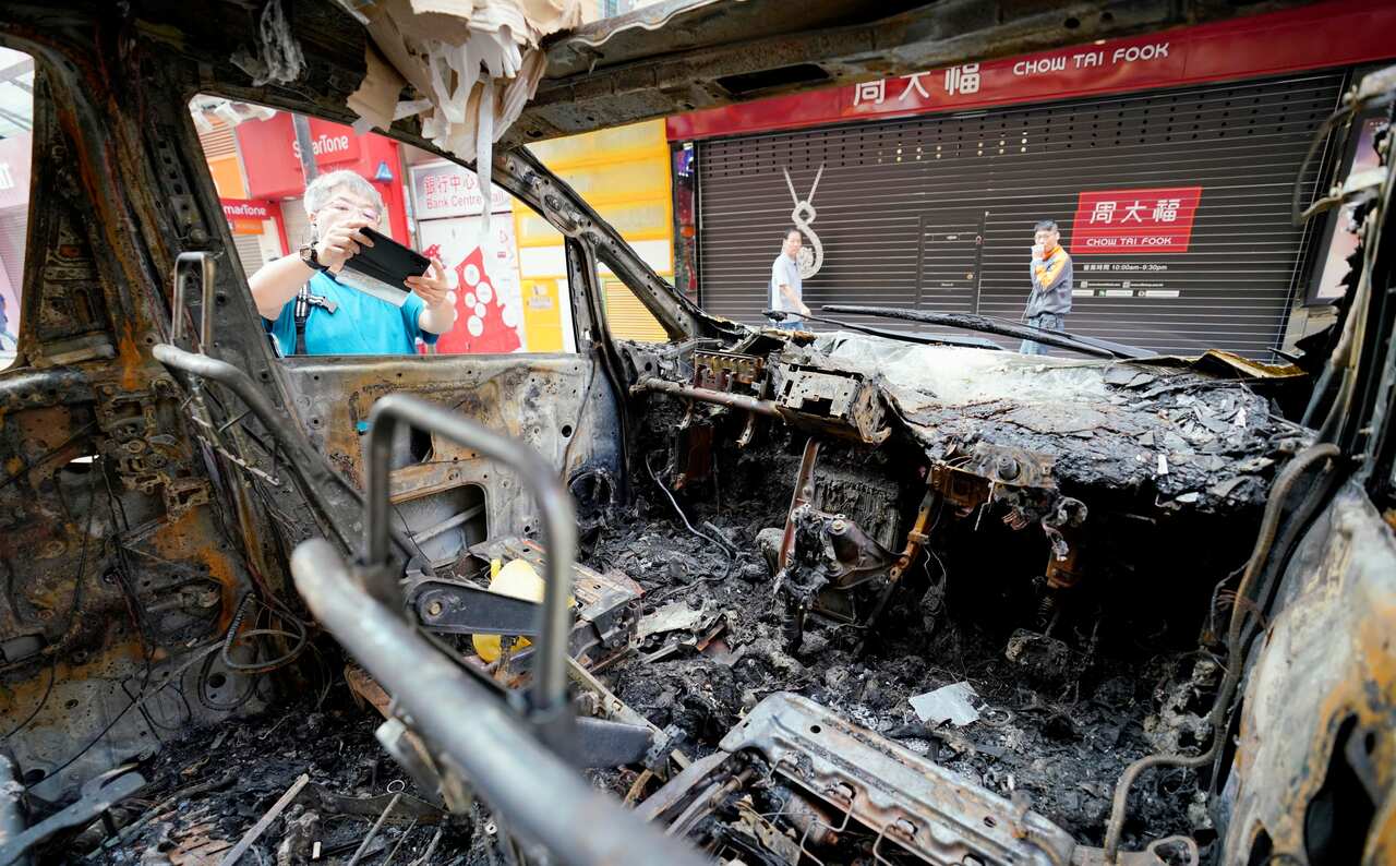 A passerby takes a picture of a burned-out car on a street in Hong Kong.