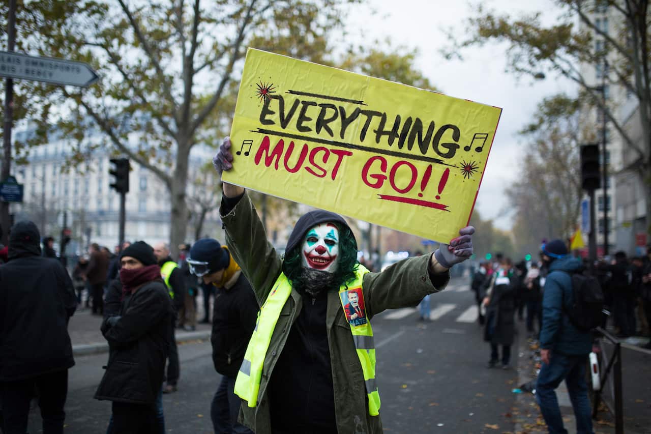 A Yellow Vest with a Joker make up holding a sign Everything must go.