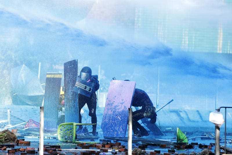 Protestors duck behind shields as a blue-dyed liquid is sprayed from an armored police vehicle at the Hong Kong Polytechnic University