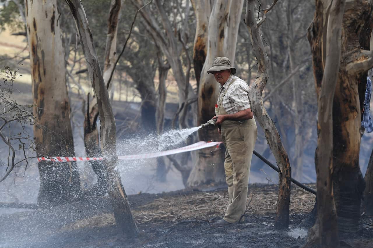 Farmer Tom Davies sprays water onto smouldering bushland at Mount Glasgow, Victoria.