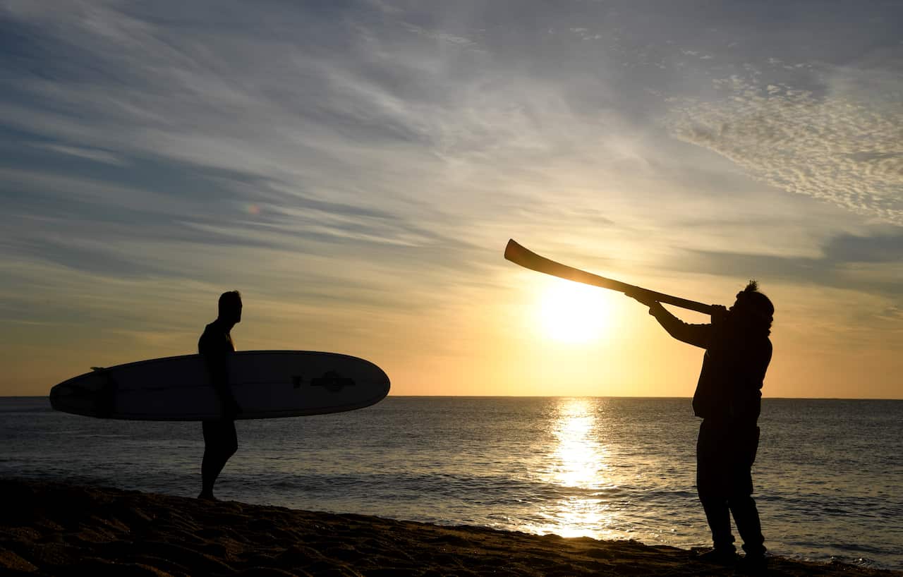 A surfer and a man playing a didgeridoo are seen as part of a protest at Bells Beach.