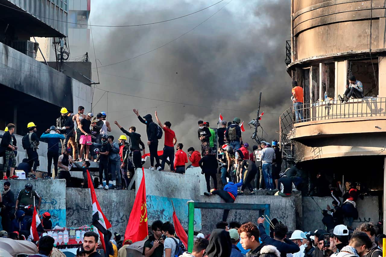 Anti-government protesters stand on a concrete wall erected by security forces to close Rasheed Street during clashes in Baghdad.