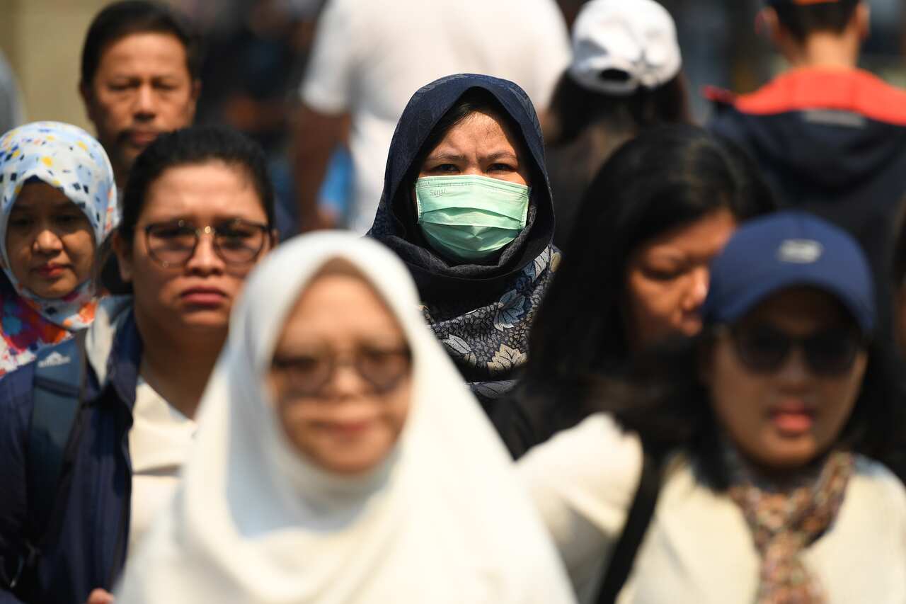 A woman seen wearing a dust mask as smoke haze from bushfires in New South Wales blankets the CBD in Sydney, Tuesday, December 3, 2019. (AAP Image/Joel Carrett) NO ARCHIVING