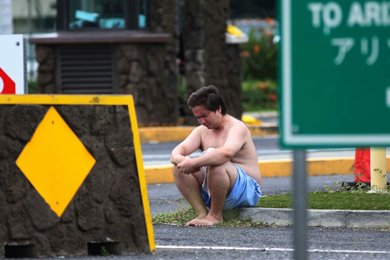 An unidentified male sits outside the the main gate at Joint Base Pearl Harbor-Hickam, Wednesday, Dec. 4, 2019, in Hawaii, following a shooting. (AP Photo/Caleb Jones)