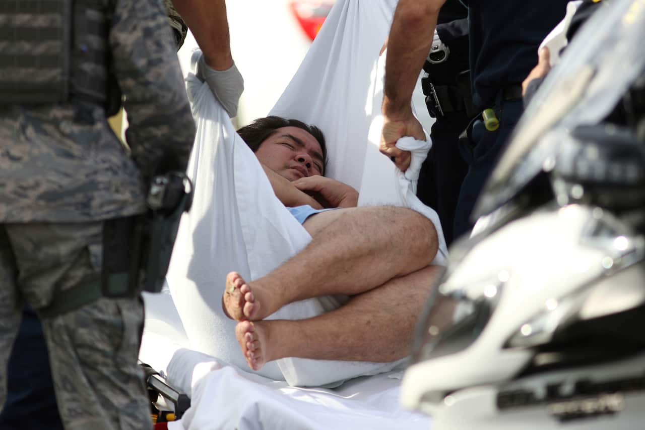 An unidentified male is taken away on a stretcher outside the main gate at Joint Base Pearl Harbor-Hickam, Wednesday, Dec. 4, 2019, in Hawaii, following a shooting. (AP Photo/Caleb Jones)