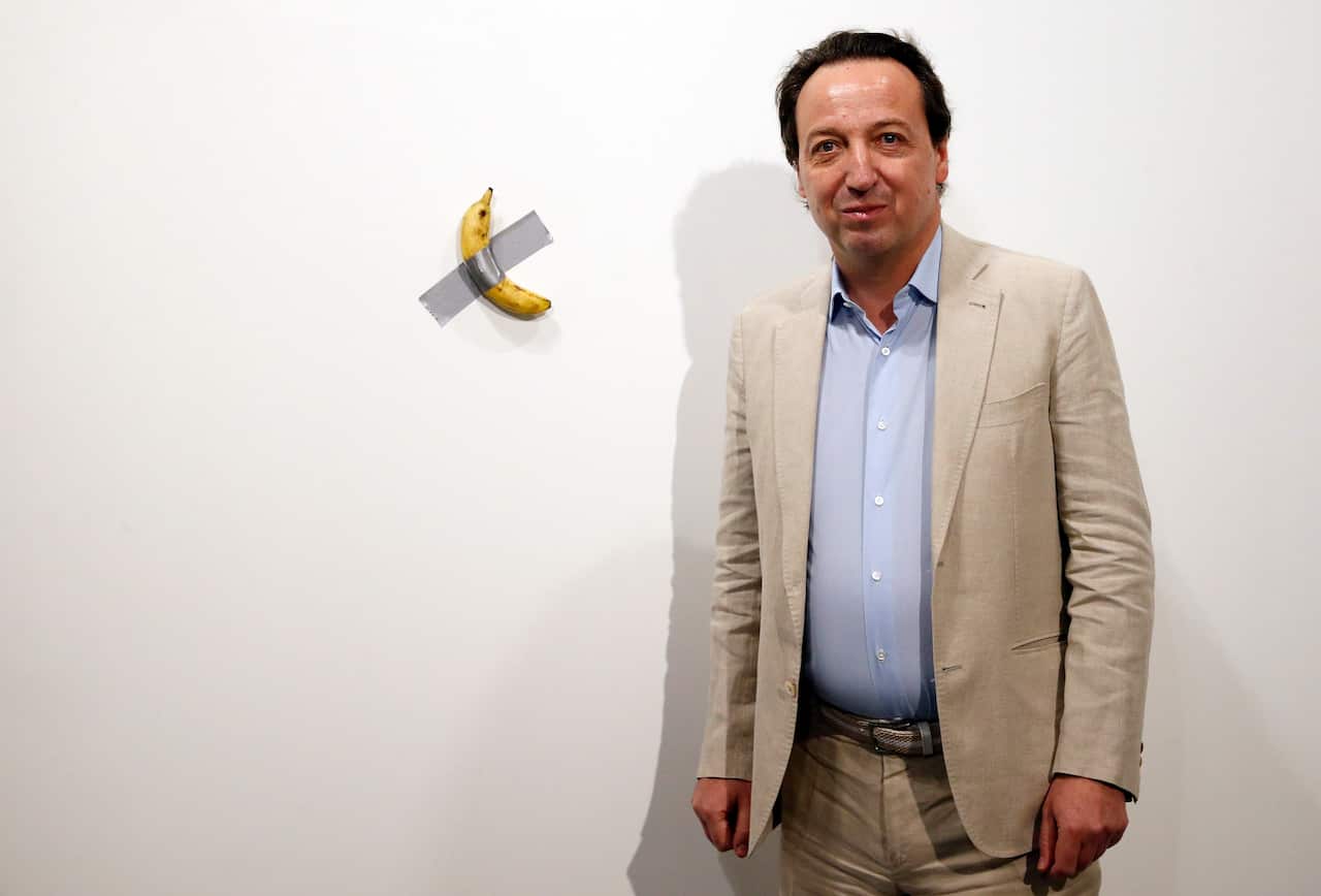 Emmanuel Perrotin, founder of the Perrotin Gallery poses with Italian artist Maurizio Cattelan piece's 'Comedian' (a banana duct taped to the wall).