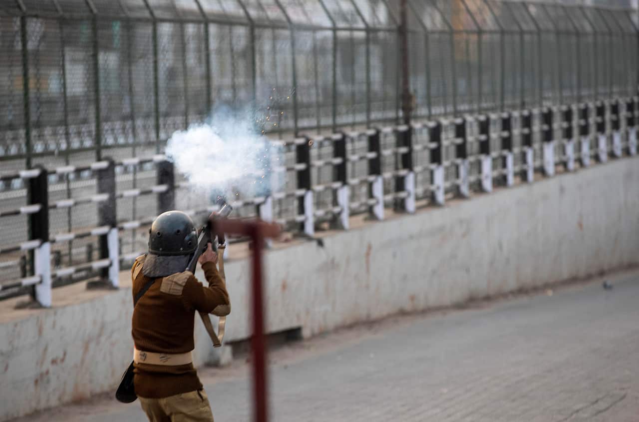An Indian policeman fires teargas at protestors during a curfew in Gauhati, India.