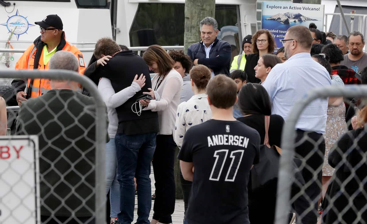 Families of victims of the White Island eruption embrace after arriving back to the Whakatane wharf following a blessing at sea.