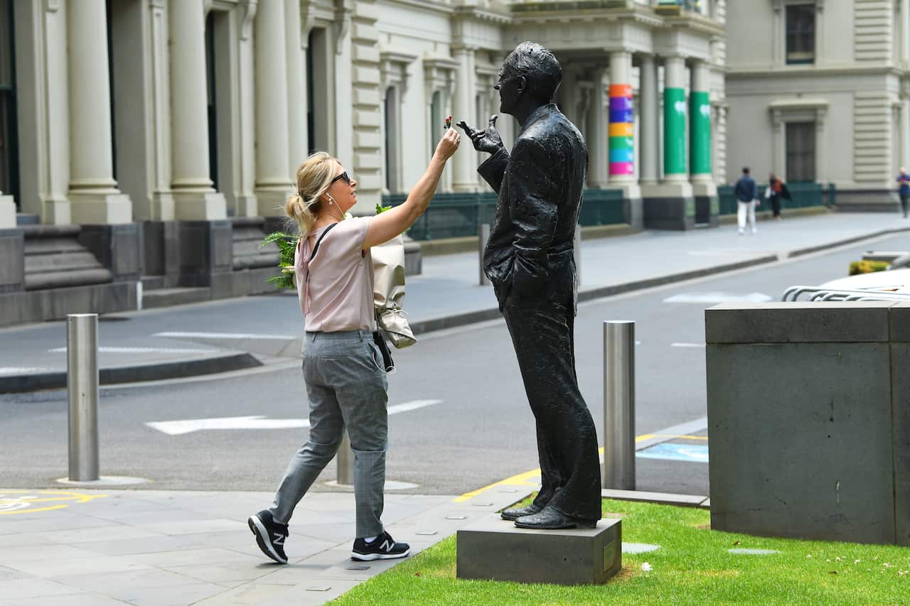 A lady places a flower onto the statue of former Victorian Premier John Cain.