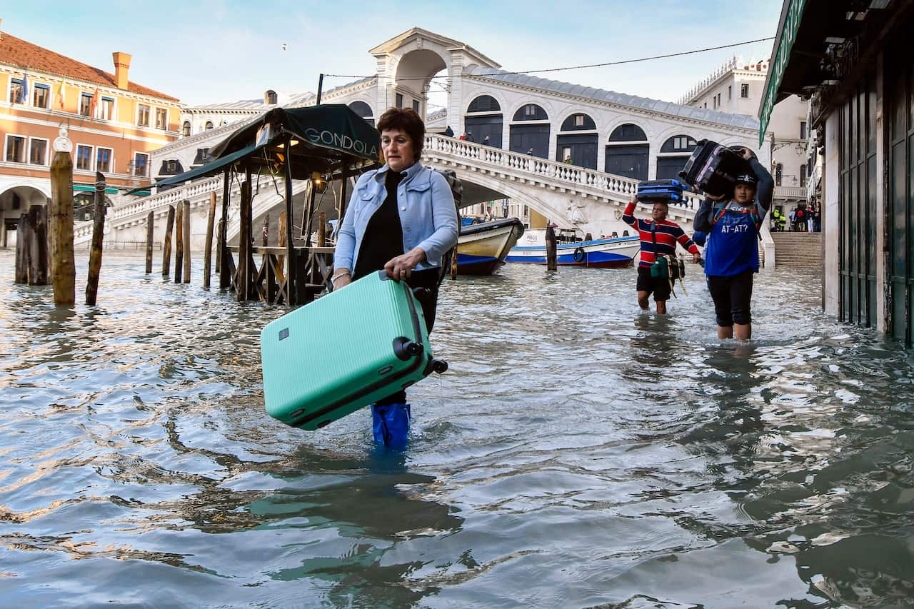 People carry their luggage as they wade through water.