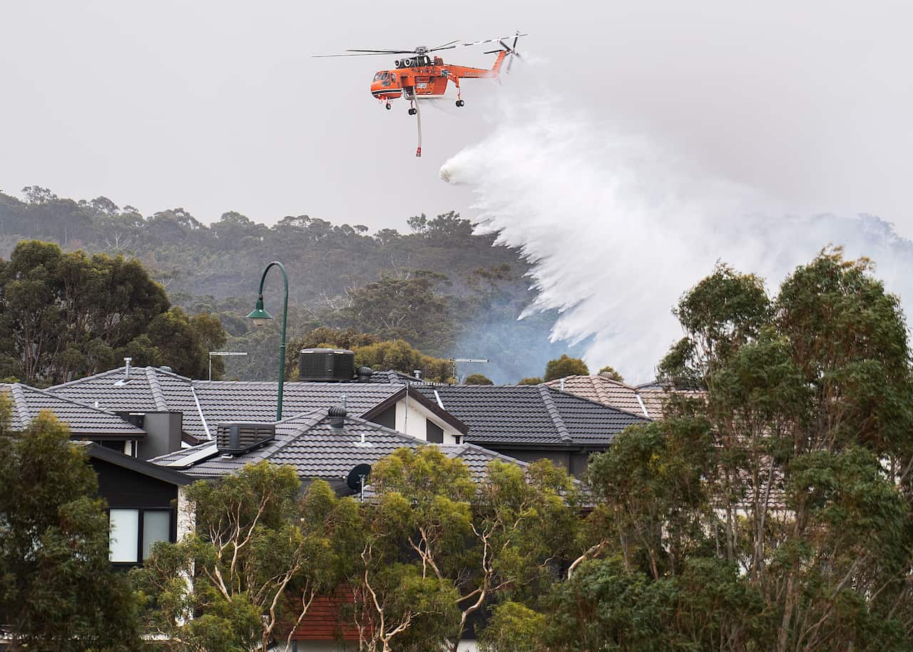 The sky crane drops water on a bushfire in scrub behind houses in Bundoora.