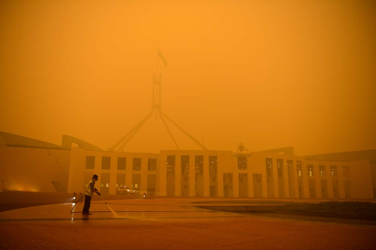A man cleans the forecourt of Parliament House surrounded by smoke haze early morning in January.