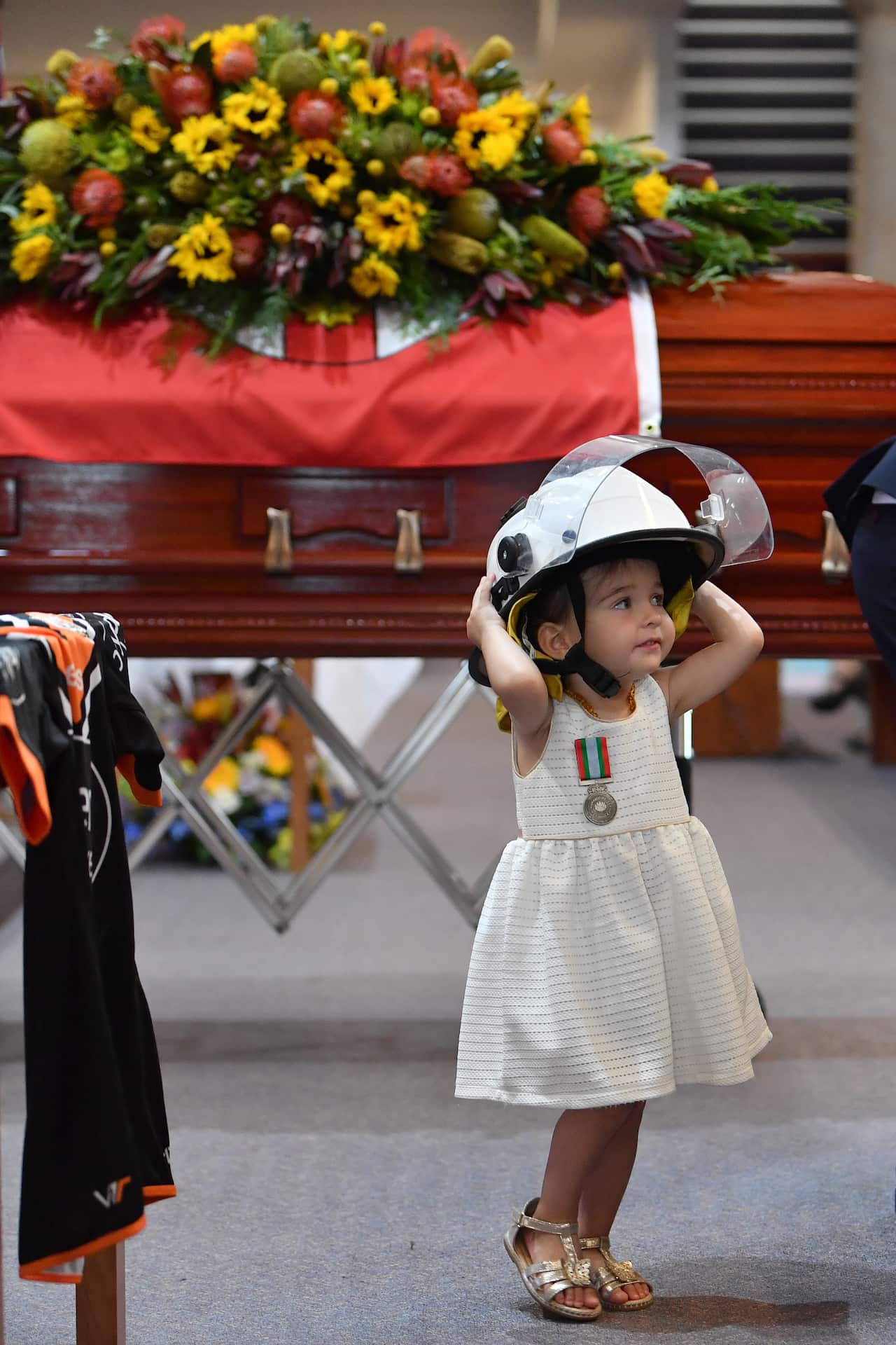 Charlotte O'Dwyer, the young daughter of Rural Fire Service volunteer Andrew O'Dwyer stands in front of her fathers casket wearing his helmet.