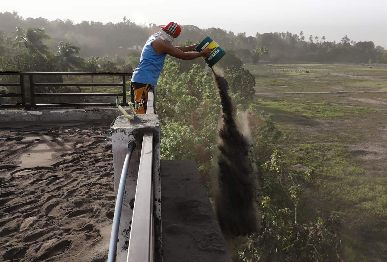 A man throws out ash deposits that accumulated on the roof of his home, a day after the eruption of Taal Volcano.