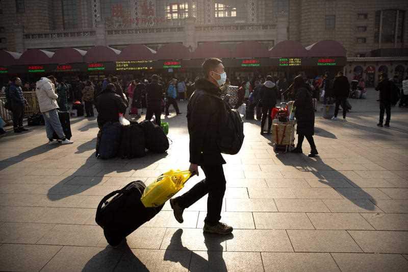 A traveler wears a facemask as he walks in front of the Beijing Railway Station in Beijing, Friday, Jan. 17, 2020
