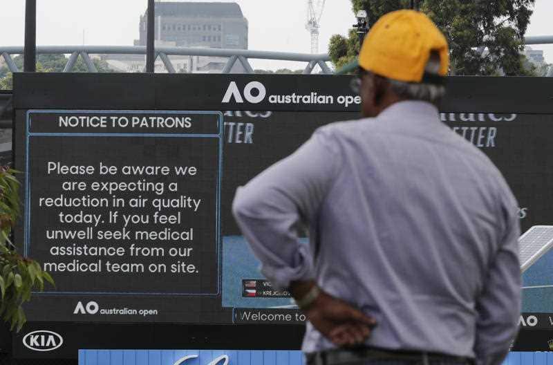 A spectator reads a sign warning of air quality ahead of the Australian Open tennis championship in Melbourne, Australia, Saturday, Jan. 18, 2020.